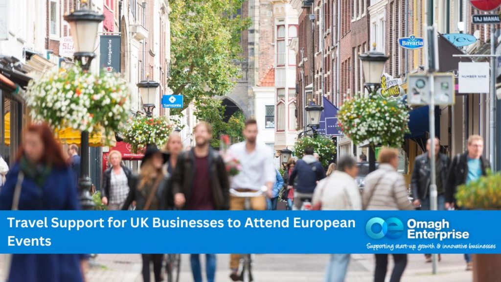 Blurred figures, walking through a busy european city street. Blue banner along the bottom. White text "Travel Support for UK Businesses to Attend European Events" Omagh Enterprise logo within the banner