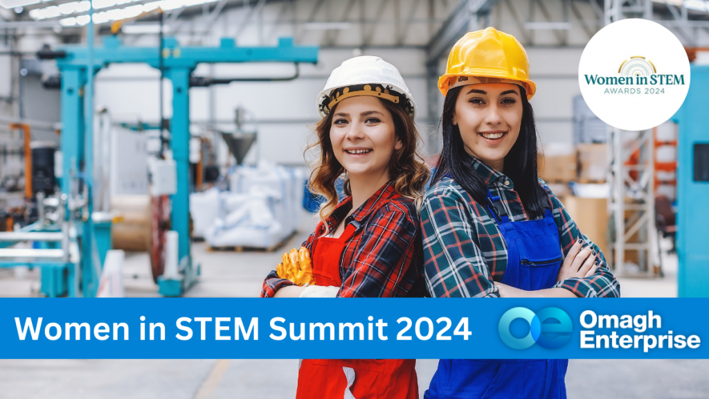 Two women standing in a factory warehouse together, both wearing hard hats. Blue banner along the bottom, with white text. "Women in STEM Summit 2024" Omagh Enterprise logo within the banner.