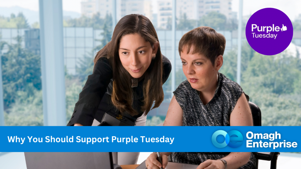 Two women working together at a desk in an office setting. One points at the computer screen, while the other sits, engaged. A Purple Tuesday logo is visible, along with text: Why You Should Support Purple Tuesday, and Omagh Enterprise.